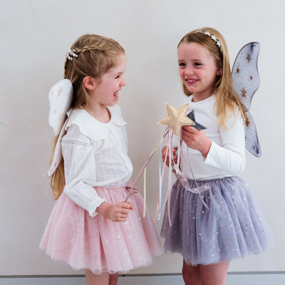 Little girl wearing grey tulle tutu speckled with gold stars and grey netted gold star print fairy wings and another wearing a pink tutu and pink wings, both with matching wands