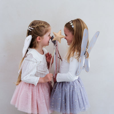 Little girl wearing grey tulle tutu speckled with gold stars and grey netted gold star print fairy wings and another wearing a pink tutu and pink wings, both with matching wands