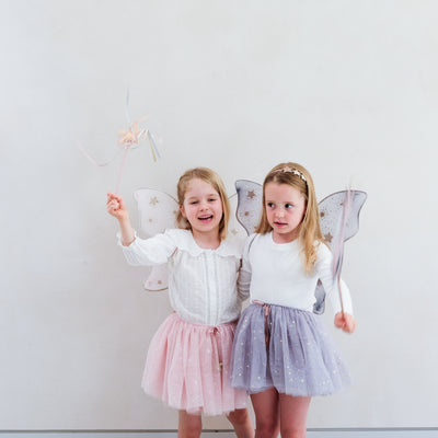 Little girl wearing grey tulle tutu speckled with gold stars and grey netted gold star print fairy wings and another wearing a pink tutu and pink wings, both with matching wands