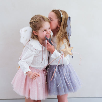 Little girl wearing grey tulle tutu speckled with gold stars and grey netted gold star print fairy wings and another wearing a pink tutu and pink wings, both with matching wands