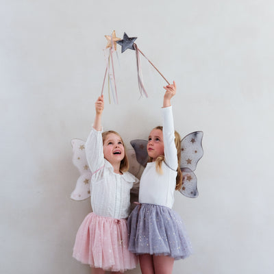 Little girl wearing grey tulle tutu speckled with gold stars and grey netted gold star print fairy wings and another wearing a pink tutu and pink wings, both with matching wands