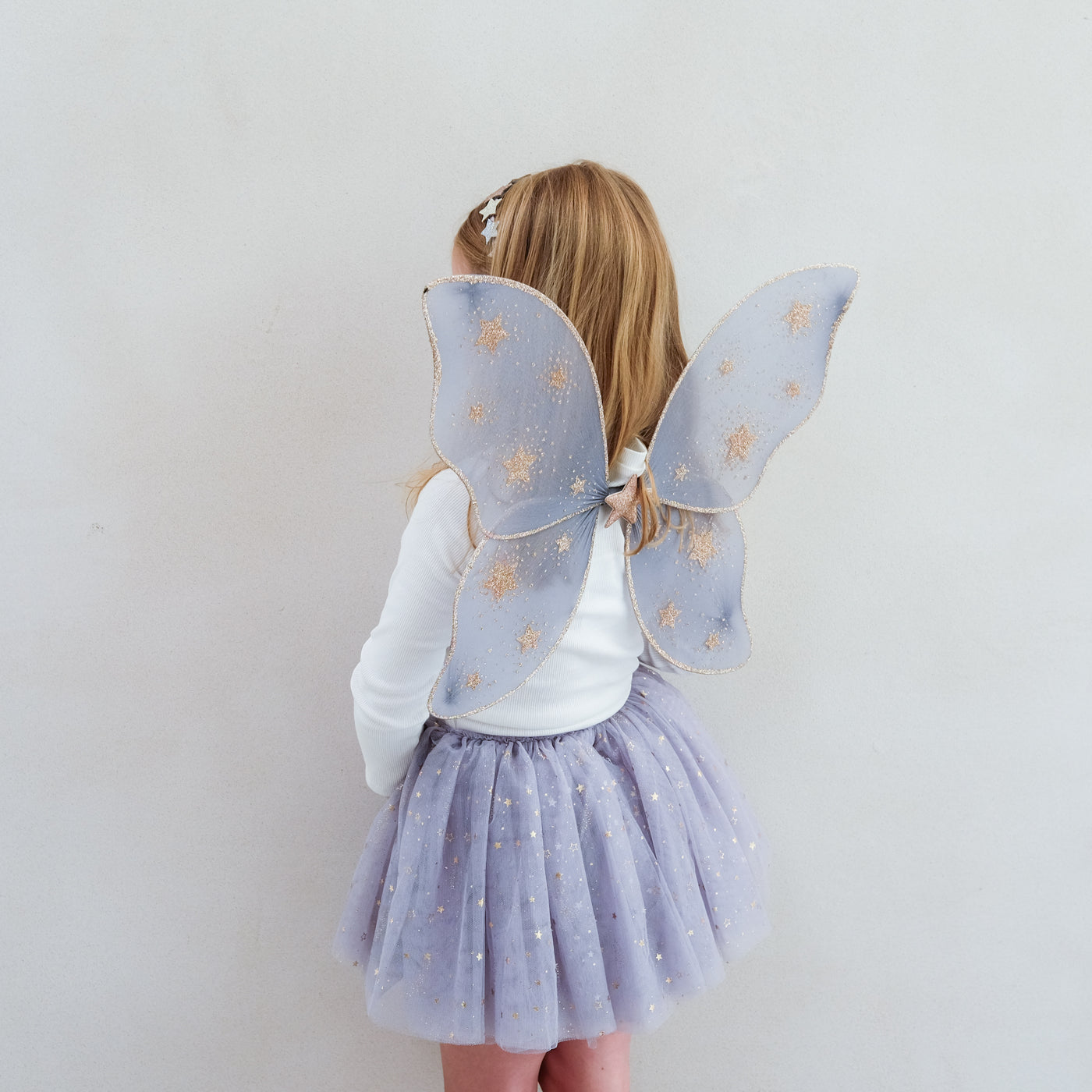 Little girl wearing grey tulle tutu speckled with gold stars and grey netted gold star print fairy wings