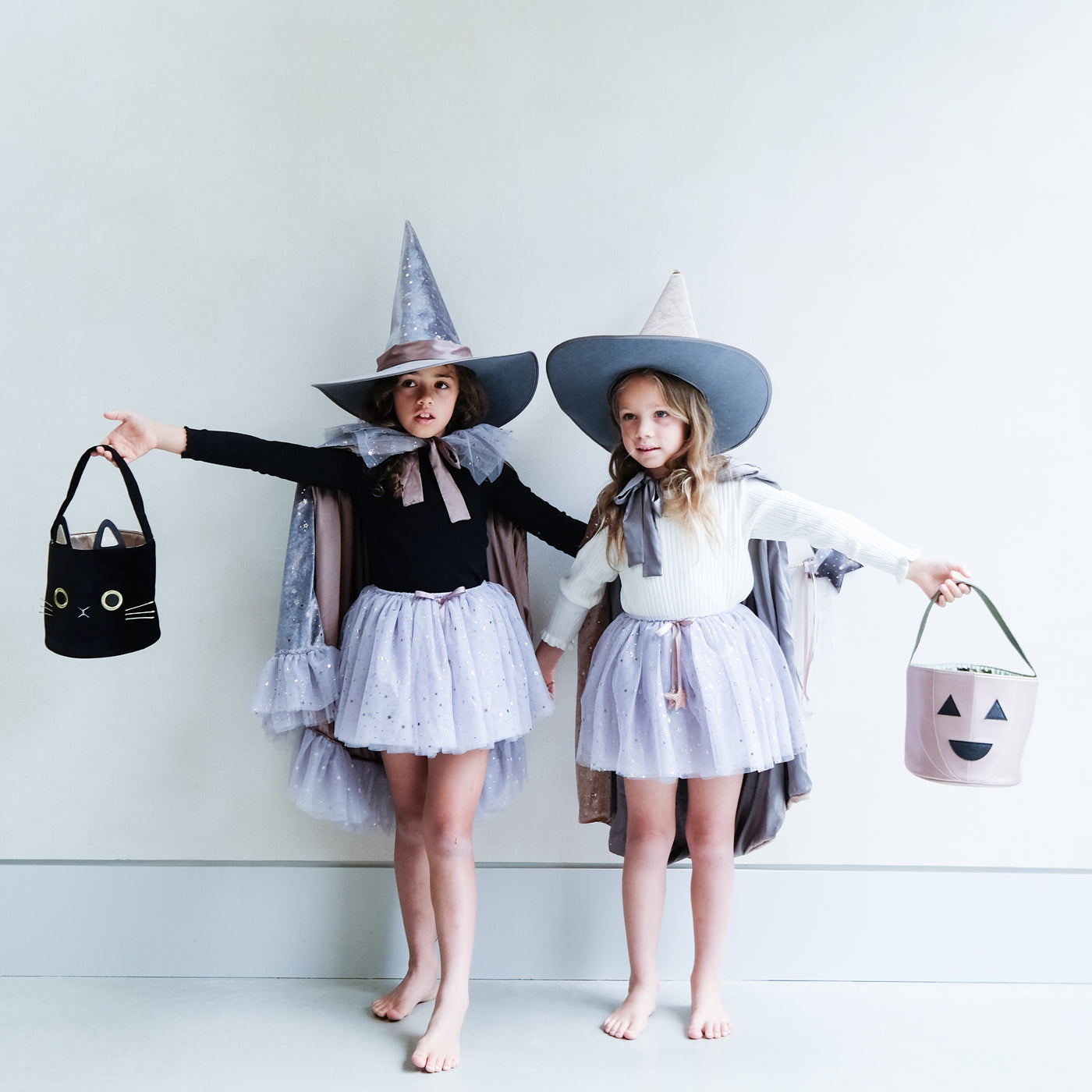 little girl holding a pumpkin trick or treat bag for halloween against a plain background