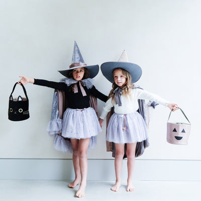 little girl holding a pumpkin trick or treat bag for halloween against a plain background