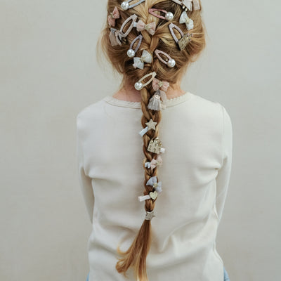 Little girl with long blonde hair in a french plait decorated with princess themed clips, pearl clips and tulle bows