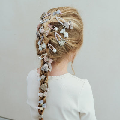 Little girl with long blonde hair in a french plait decorated with princess themed clips, pearl clips and tulle bows