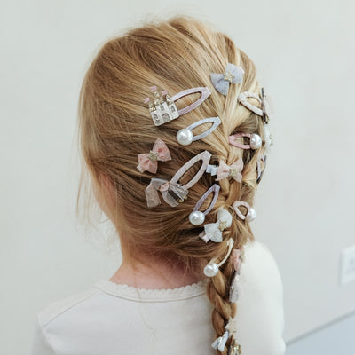 Little girl with long blonde hair in a french plait decorated with princess themed clips, pearl clips and tulle bows
