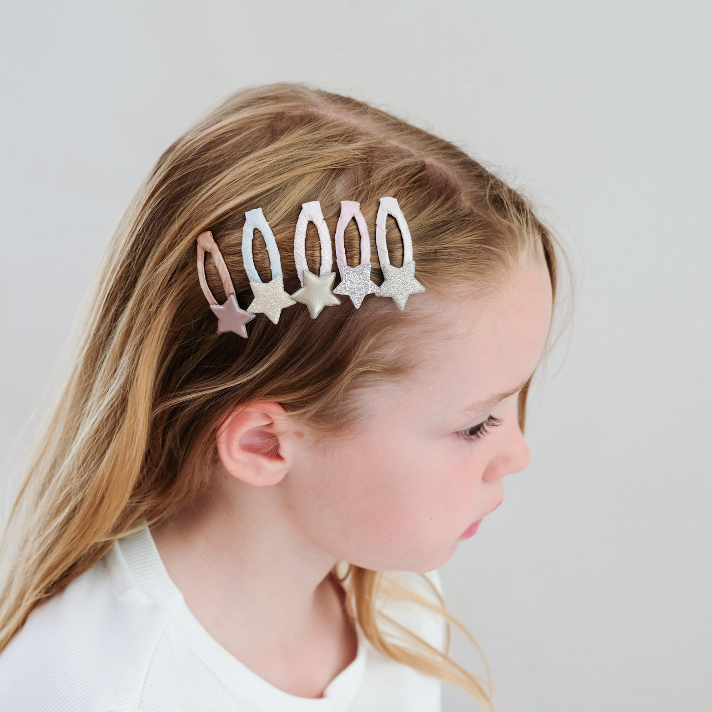 Five pack of mini star hair clips worn to the side of young dark blonde child - glitter and metallic fabrics