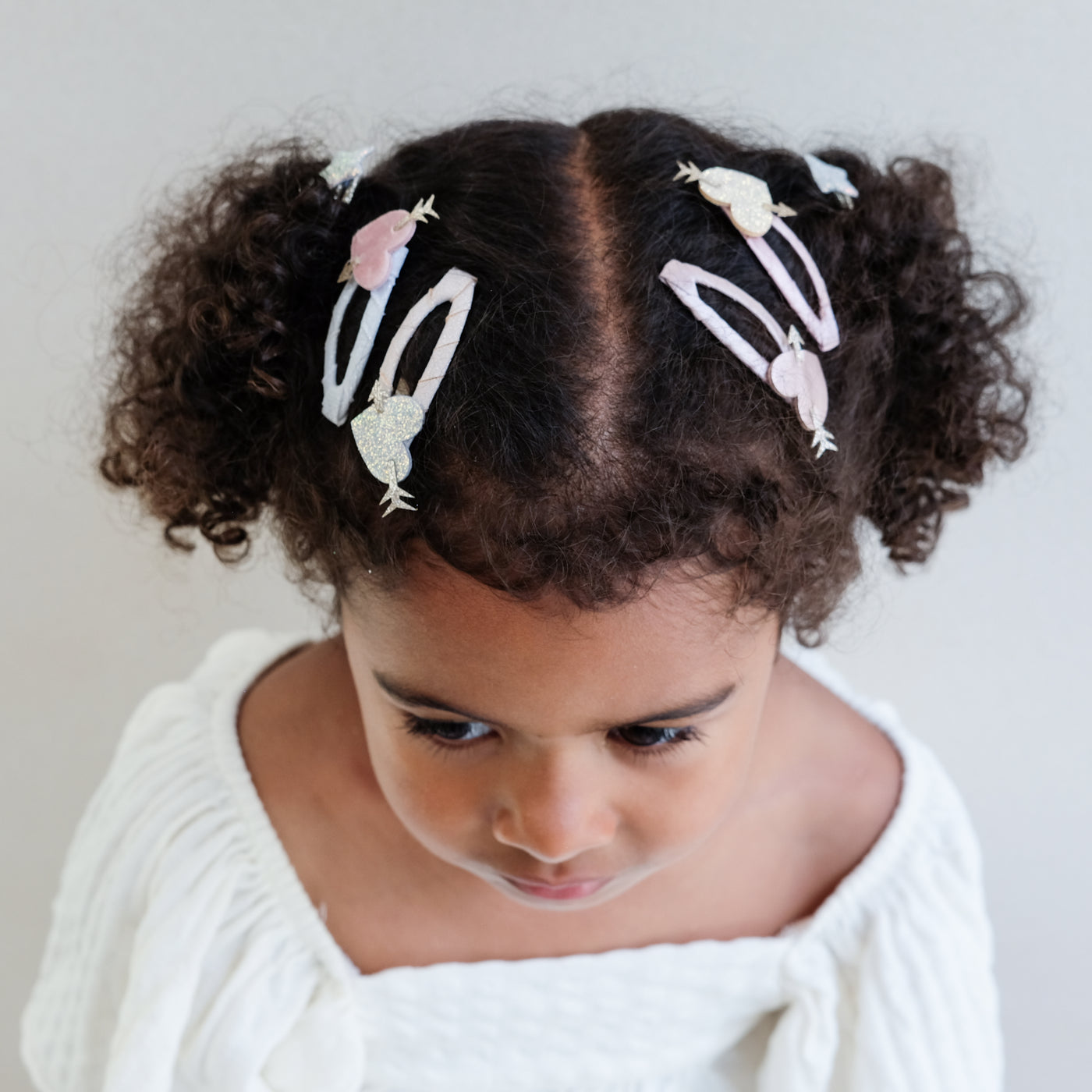 Dark haired girl wearing heart shaped hair clips with glitter arrows