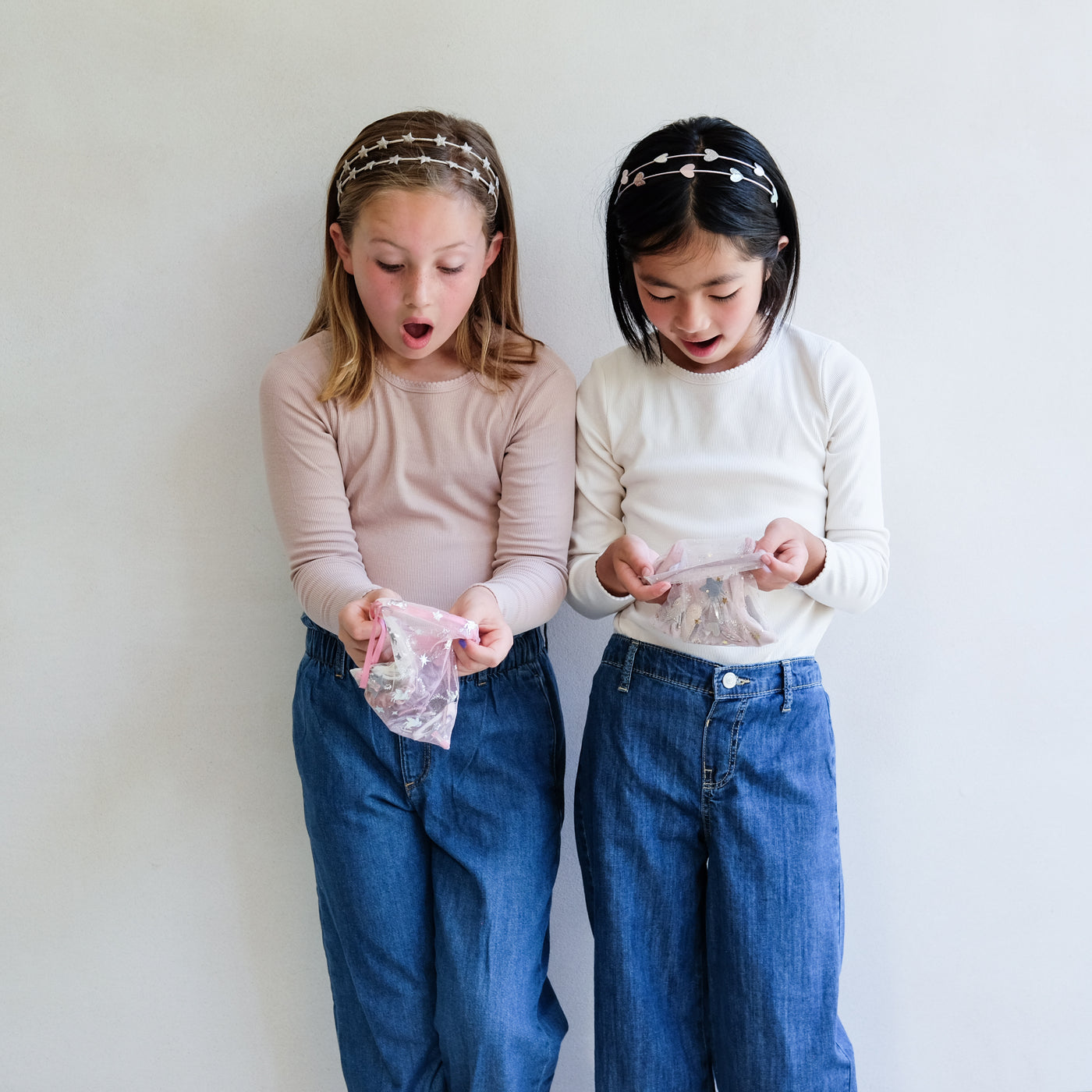 two girls holding hair accessory gift bags against a white background
