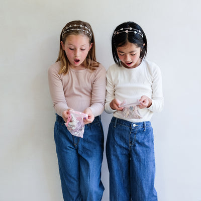 two girls holding hair accessory gift bags against a white background