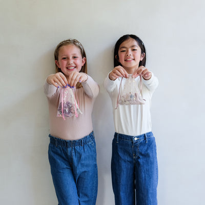 two girls holding hair accessory gift bags against a white background