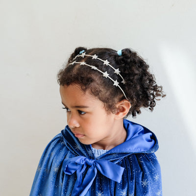 Young girl wearing a blue velvet cape with a star headband against a plain background