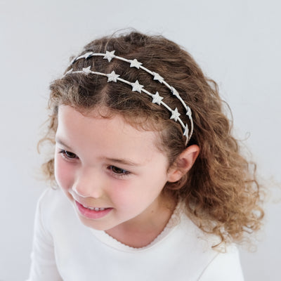 Young girl wearing a star-patterned headband against a plain background