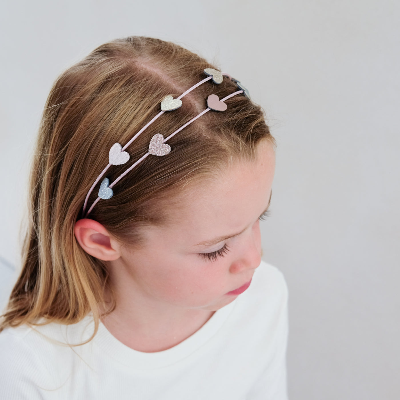 young girl wearing a heart double alice band against a white background