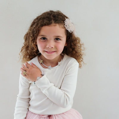 Young girl with curly hair wearing a star necklace, star ring and star bracelet in a white sweater and pink skirt against a plain background