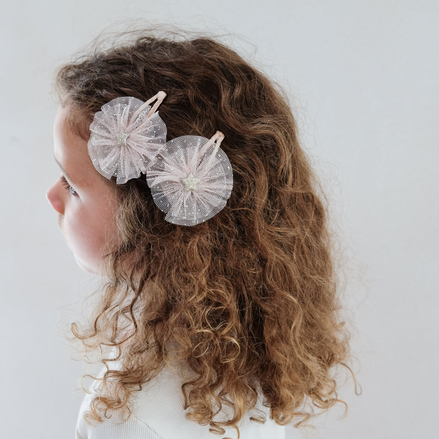 girl wearing ballerina star tulle hair clips in her hair against a white background