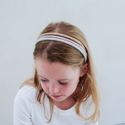 young girl wearing a pack of three glitter alice bands against a plain background
