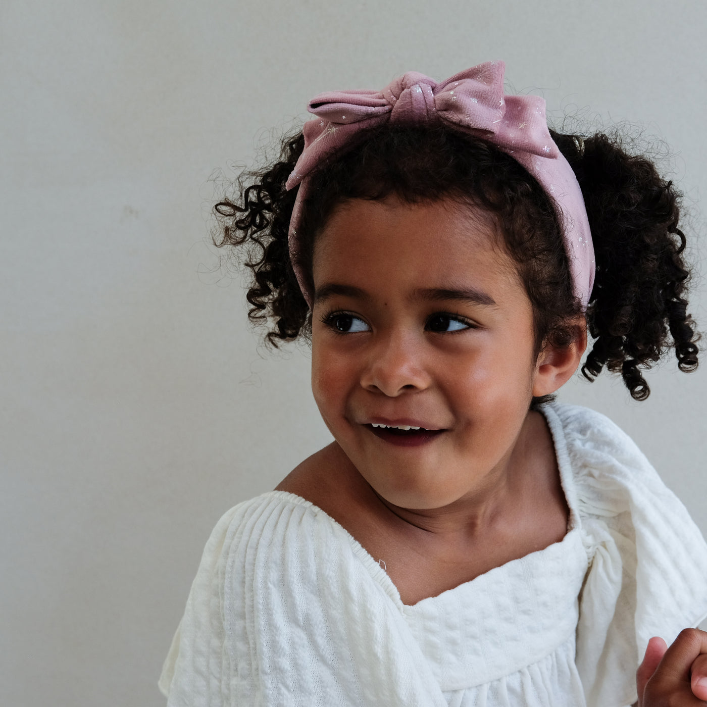 Young girl wearing a pink velvet bow shimmer headband against a plain background
