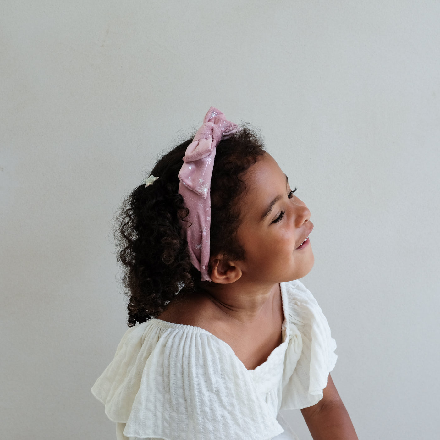 Young girl wearing a pink velvet bow shimmer headband against a plain background