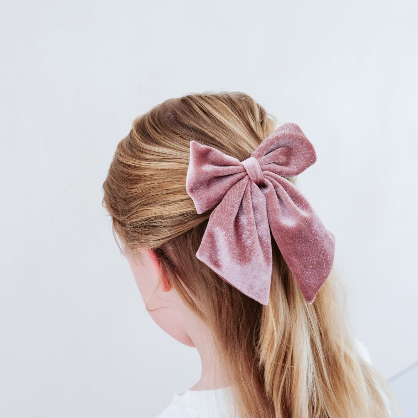girl wearing pink velvet agnes oversized bow hair clip in her hair against a white background