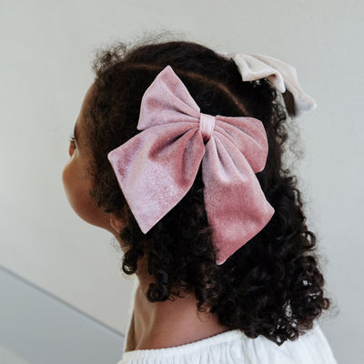 girl wearing pink velvet agnes oversized bow hair clip in her hair against a white background