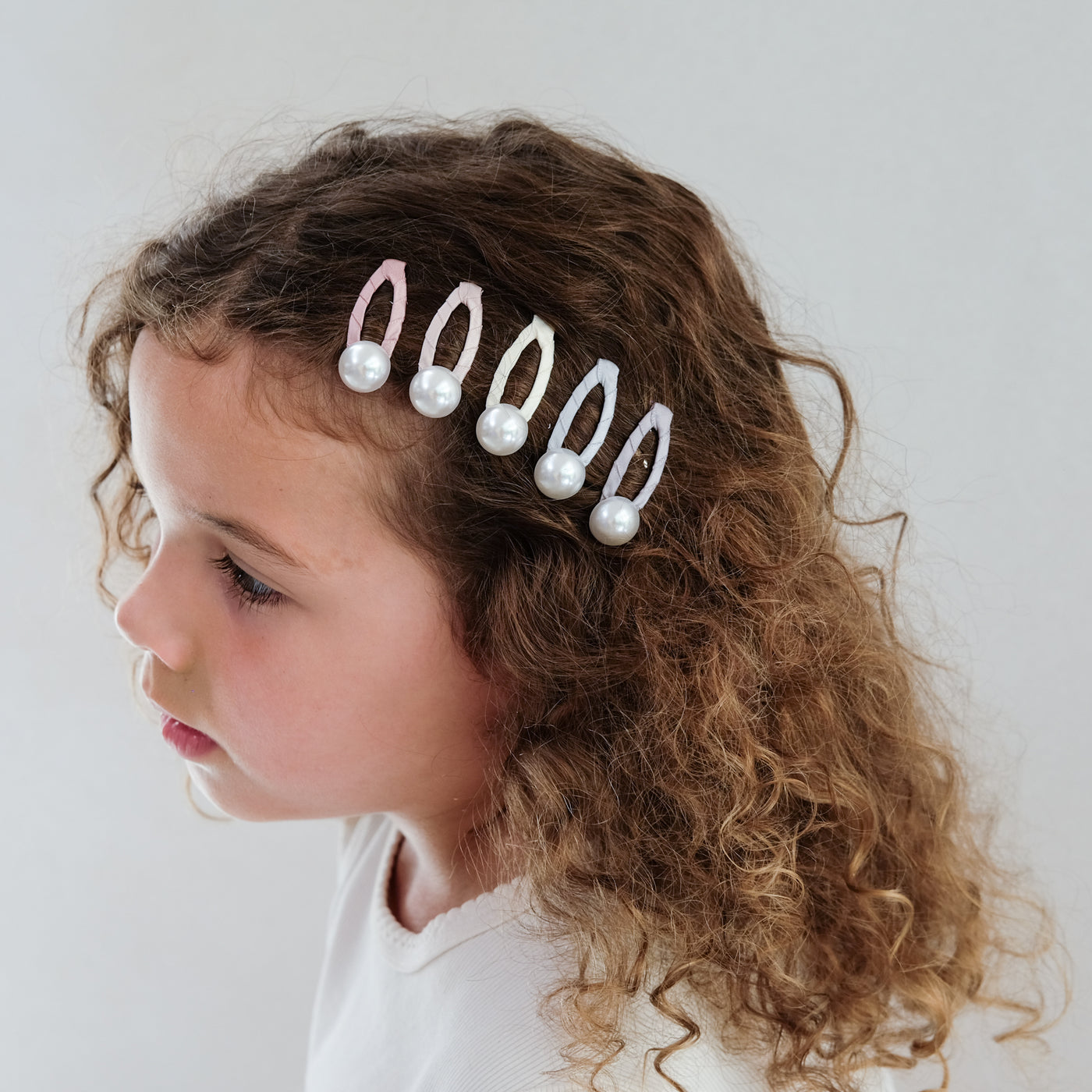 girl wearing pearly hair clips in her hair against a plain background