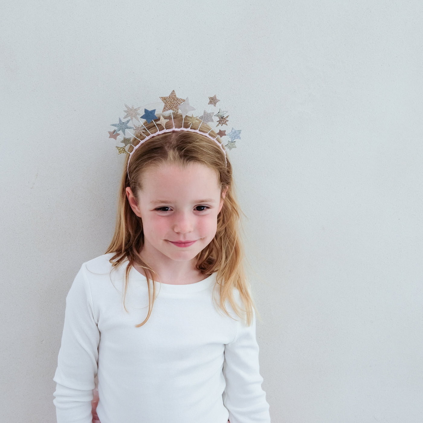 Young girl wearing a decorative star headband against a plain background