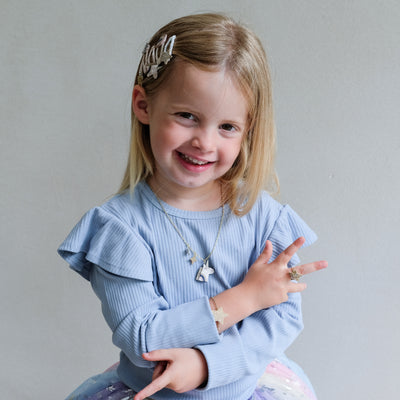 Young girl wearing a blue sweater with ruffled sleeves, smiling against a plain background