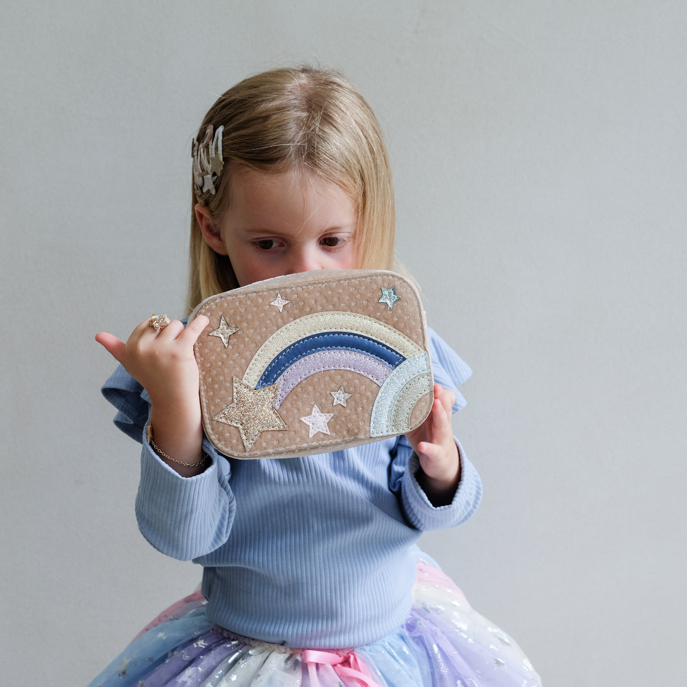 Child holding a bag with rainbow and star design against a plain background