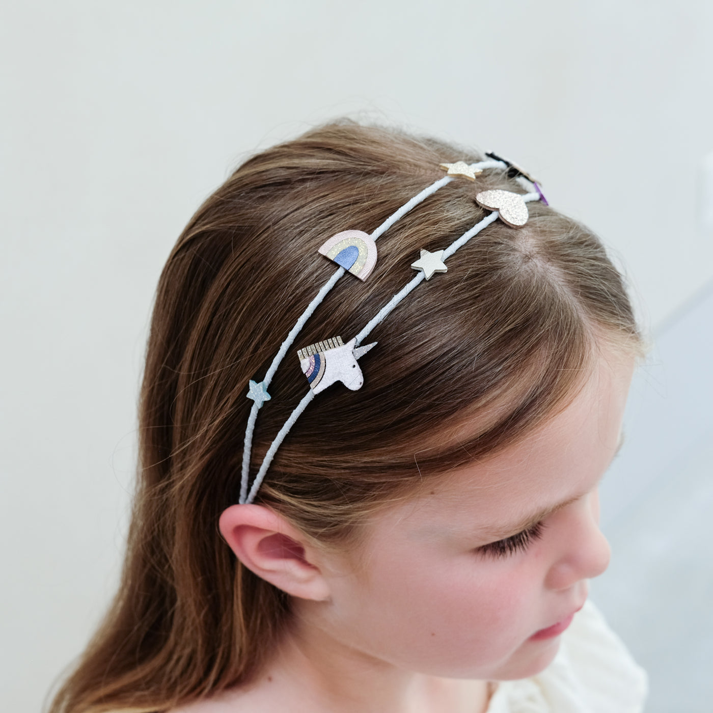 Child wearing a unicorn headband with stars and a rainbow on a plain background