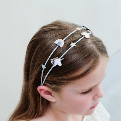 Child wearing a unicorn headband with stars and a rainbow on a plain background