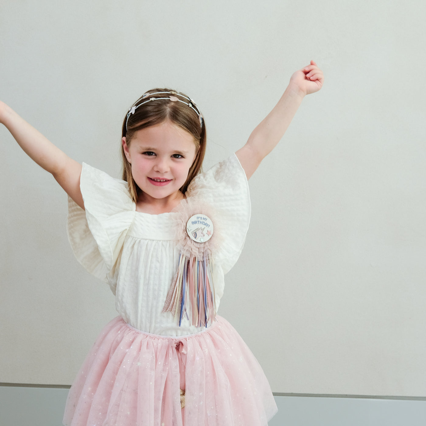 young girl wearing a unicorn happy birthday rosette badge against a plain background