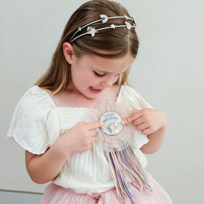 young girl wearing a unicorn happy birthday rosette badge against a plain background