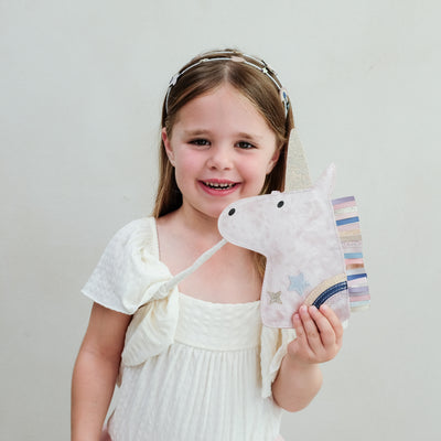Young girl holding a unicorn cross body bag against a plain background
