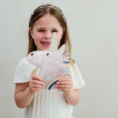 Young girl holding a velvet unicorn bag against a plain background