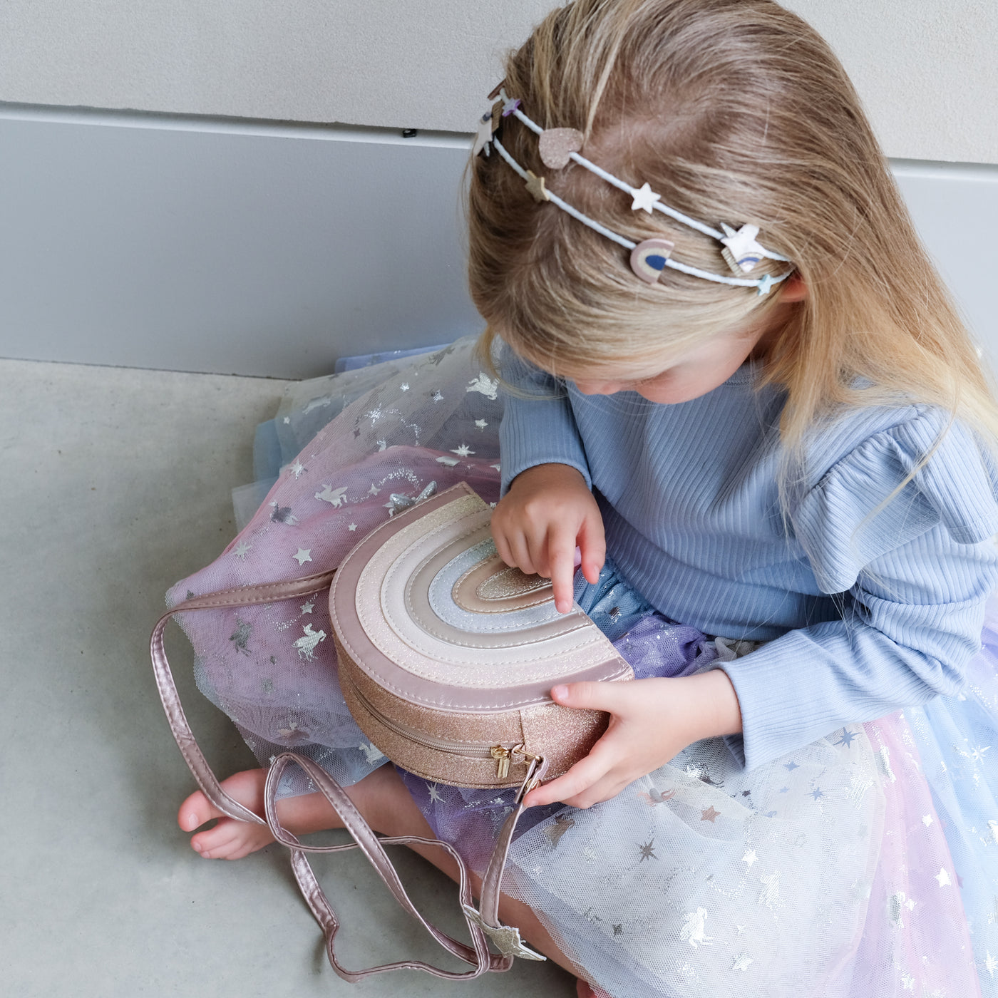 young girl holding a pink rainbow bag against a plain background
