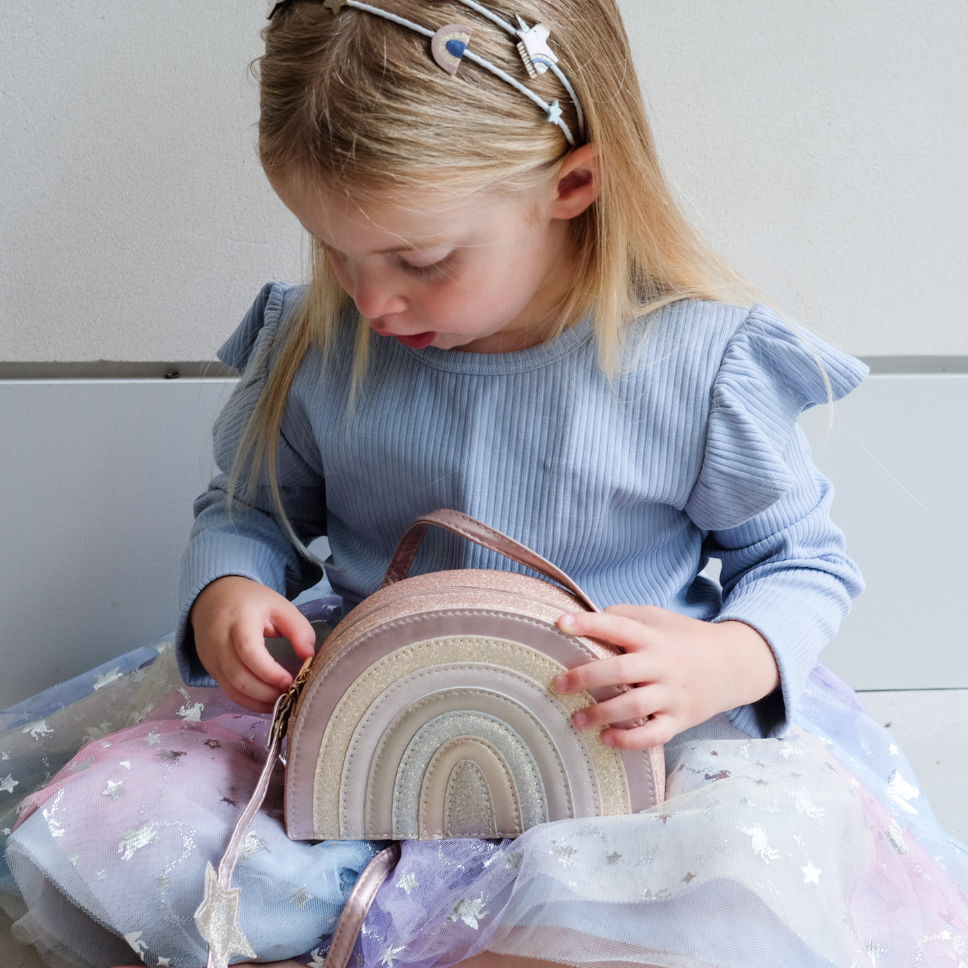 young girl holding a pink rainbow bag against a plain background