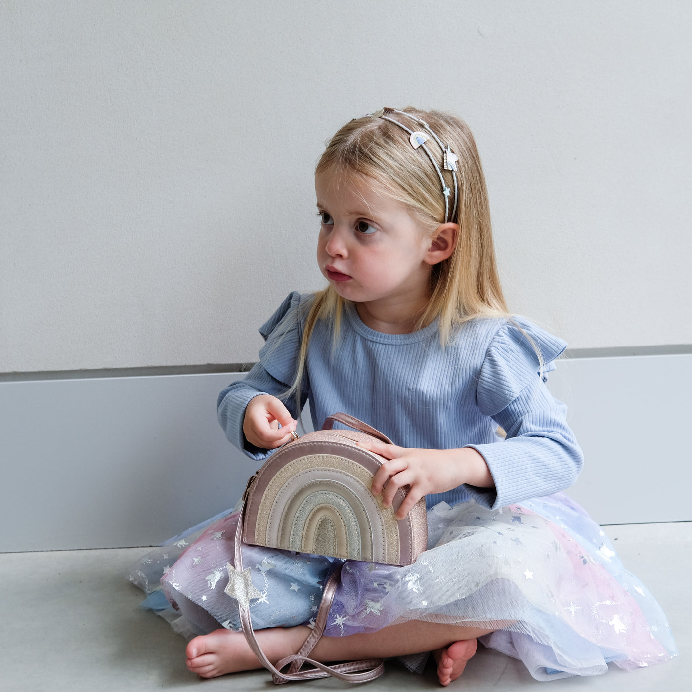 young girl holding a pink rainbow bag against a plain background