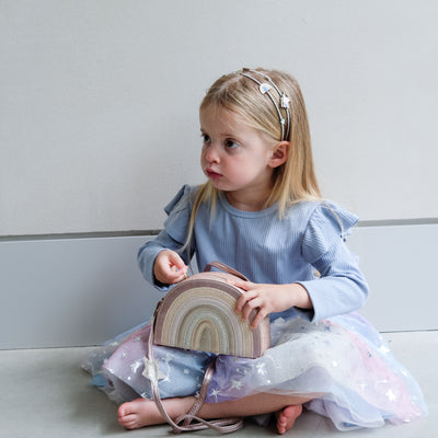 young girl holding a pink rainbow bag against a plain background
