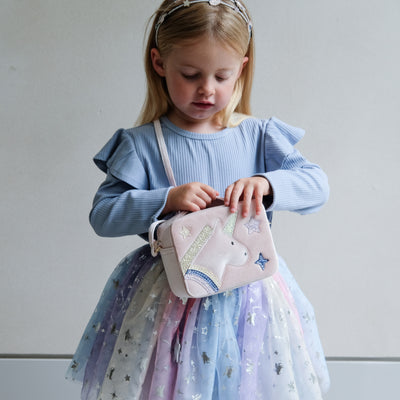 Young girl holding a pink unicorn bag against a plain background