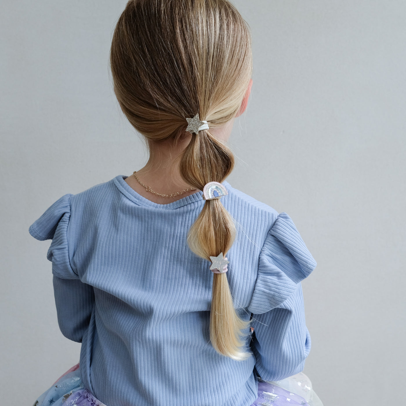 girl wearing rainbow & star ponies in hair against a white background