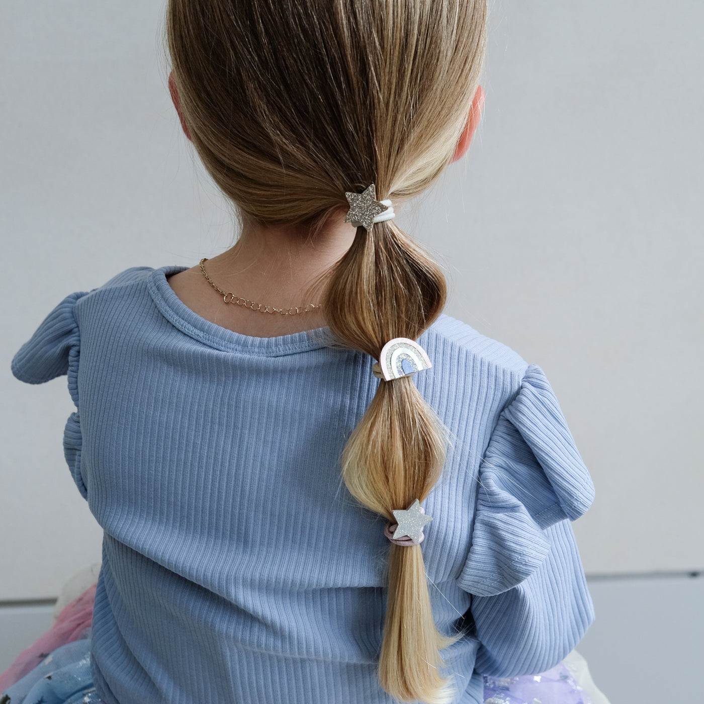 girl wearing rainbow & star ponies in hair against a white background