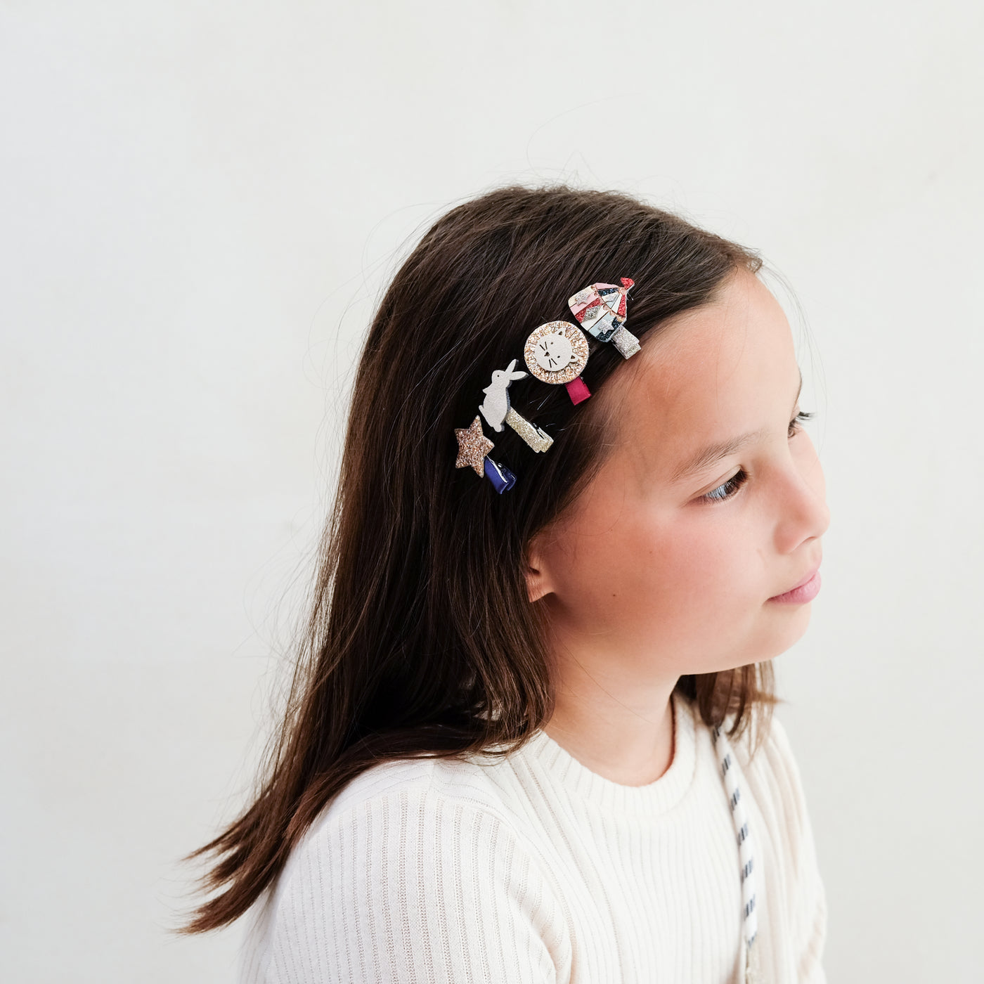 young girl wearing circus mini clips in her hair against a plain background
