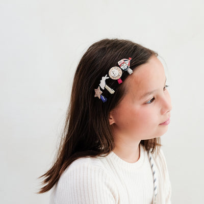 young girl wearing circus mini clips in her hair against a plain background