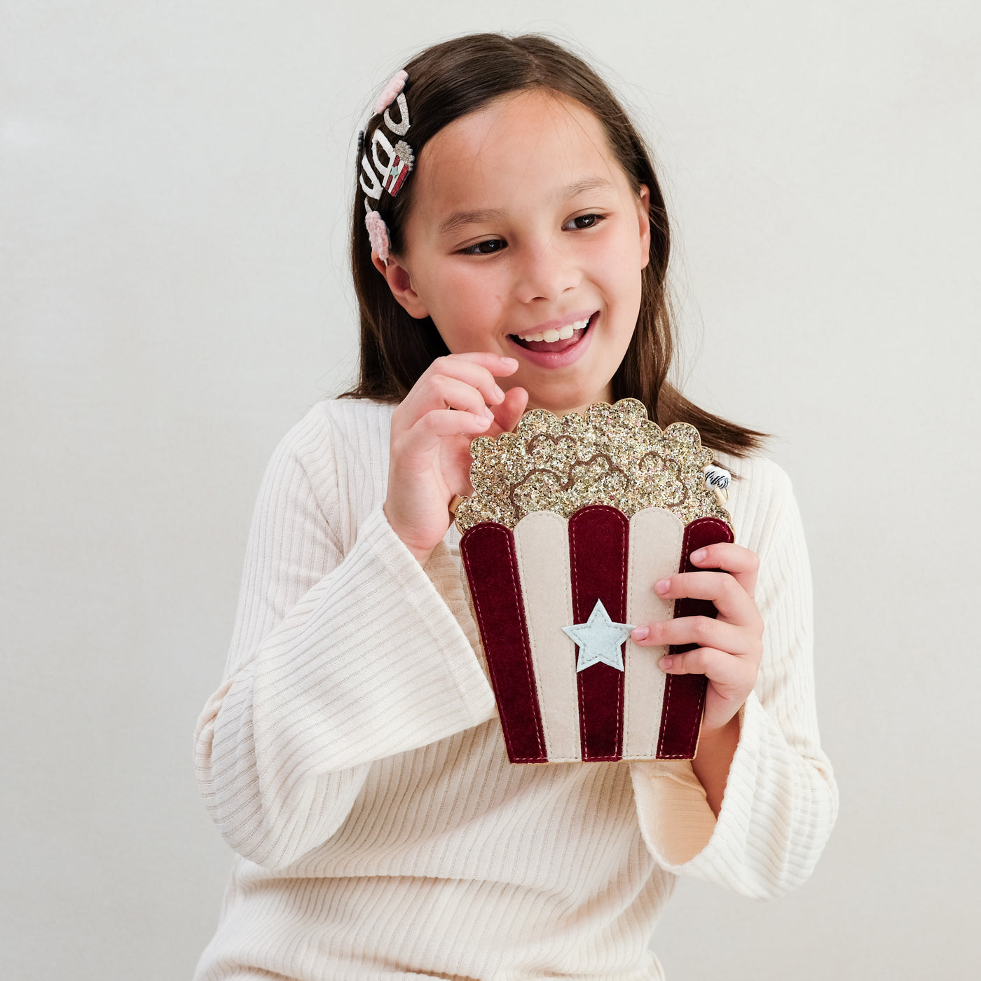 Young girl holding a decorative popcorn bag with a star design on a plain background