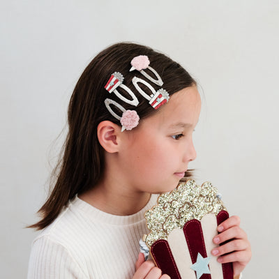 Young girl with decorative popcorn and candyfloss hair clips holding a decorative popcorn bag against a plain background