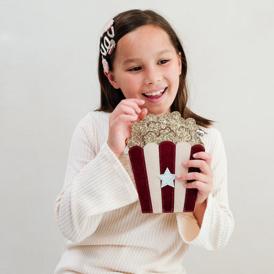 Young girl holding a decorative popcorn bag with a star design on a plain background