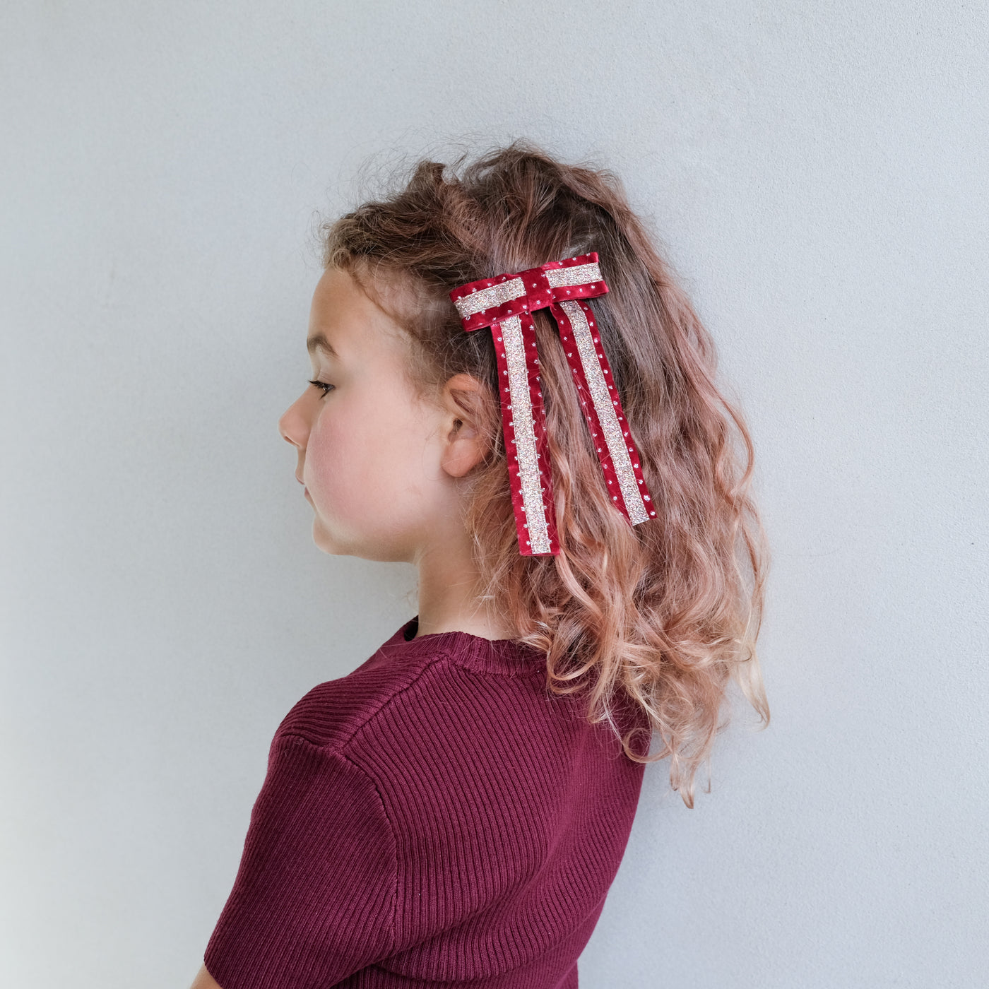 girl wearing red circus bow hair clip in her hair against a white background