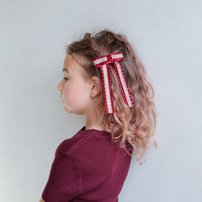 girl wearing red circus bow hair clip in her hair against a white background
